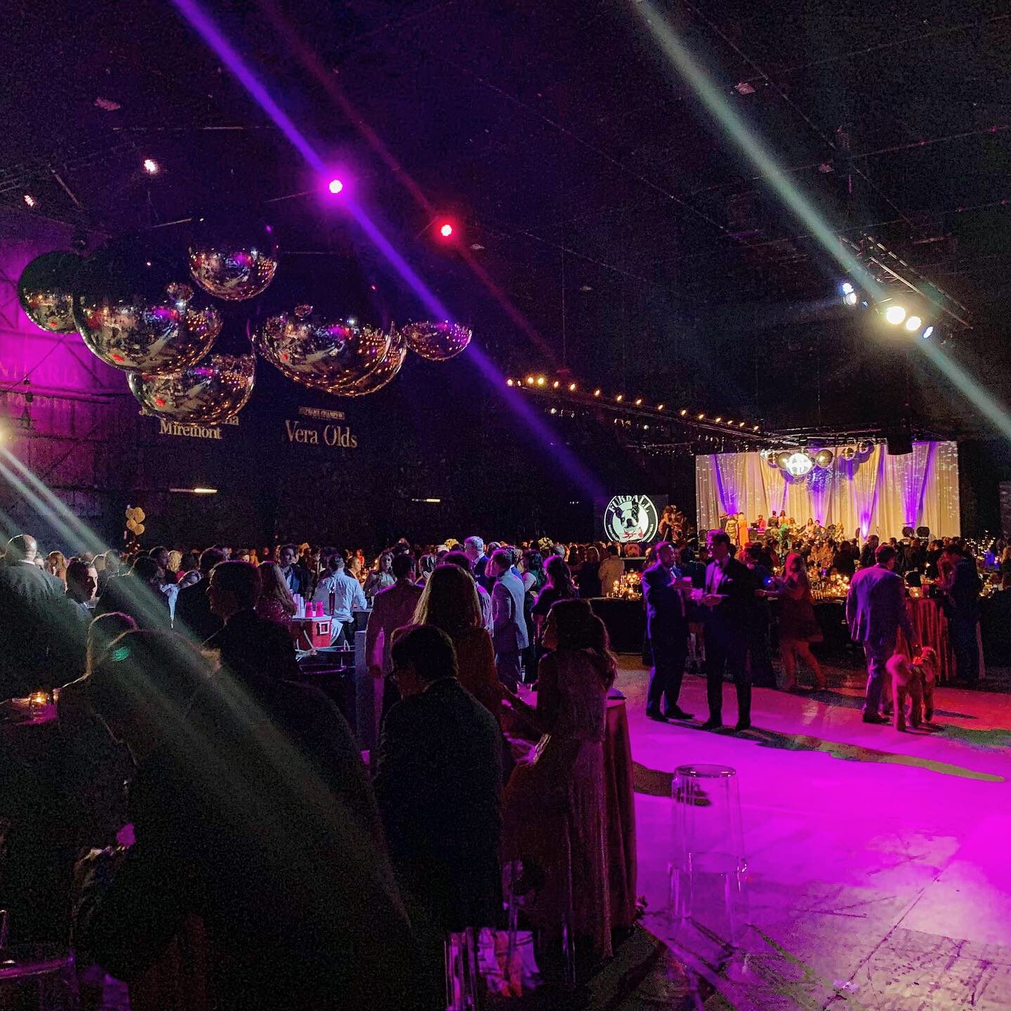 Packed event floor under mirror balls and saturated pink stage lighting