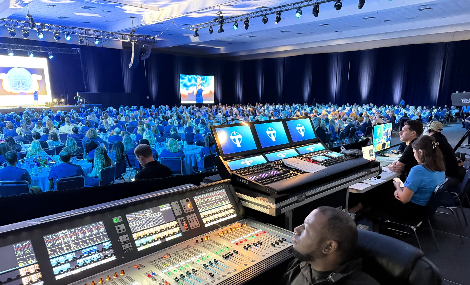 Abstract Productions engineer mixing a live event on a Soundcraft audio console beside a grandMA lighting desk in the front-of-house production booth