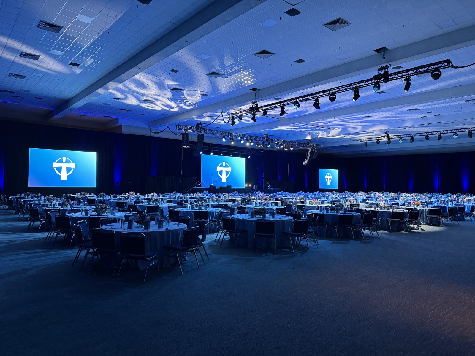 Corporate gala ballroom with blue uplighting, projection screens and banquet rounds