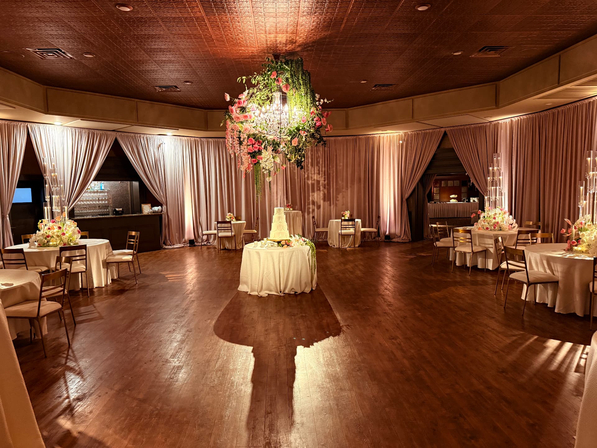 Blush full-perimeter drape with tied-back entry panels and warm uplighting in a wedding ballroom