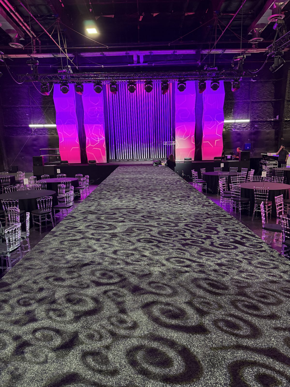 Runway stage framed by pink-lit pipe and drape panels