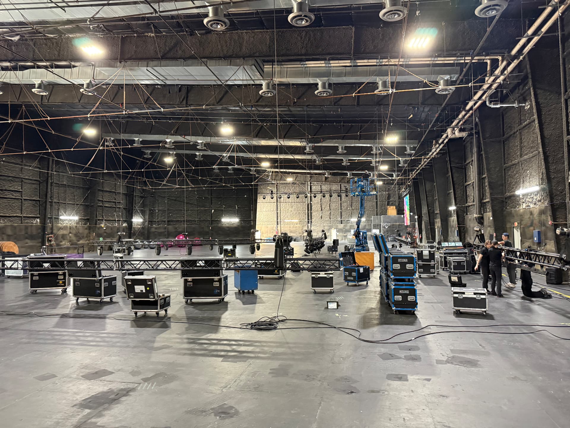 Staging load-in: trussing, road cases and a scissor lift prepped on a dark soundstage floor
